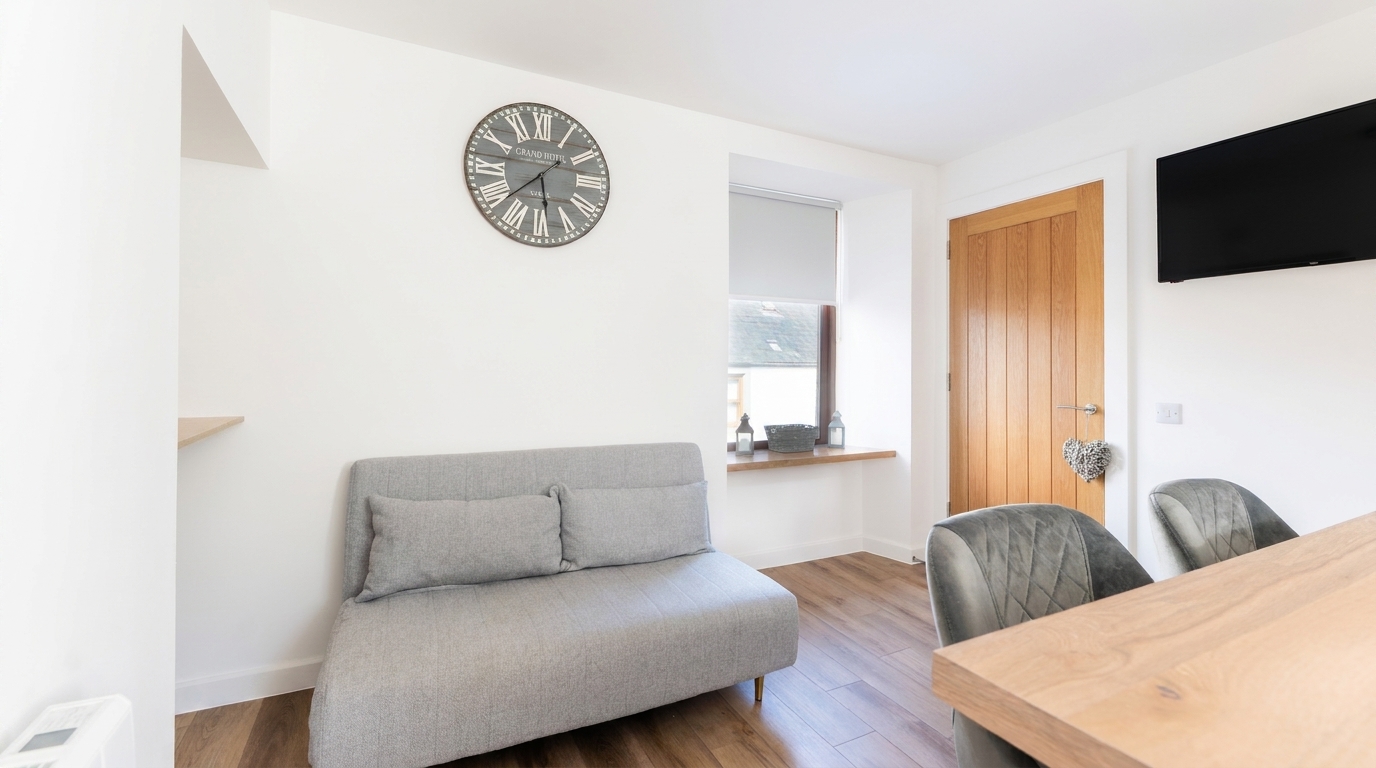 An open-plan living and dining area in a new build, with a sofa, dining table and wall-mounted television, by Groat Construction.
